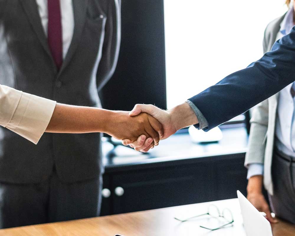 Black-and-white photo of woman shaking man's hand while 2 others look on